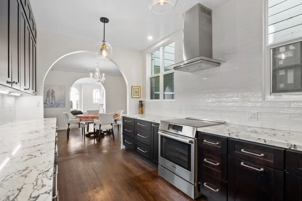 Bright modern kitchen with white cabinetry, oversized island, pendant lighting, and warm wood flooring.