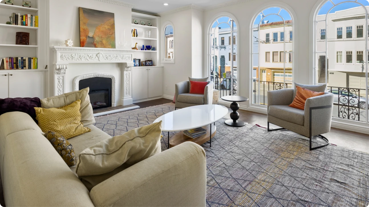 Light-filled Bay Area living space with arched street-facing windows, soft seating, and intricate fireplace detail after remodel