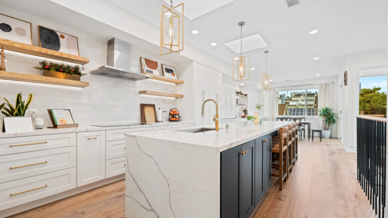 Bright modern San Francisco kitchen remodel with large white waterfall island, wood shelving, brass pendants, and open dining connection