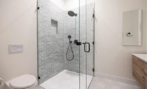 Contemporary bathroom shower with gray subway tile, black matte fixtures, and geometric floor tile detail.