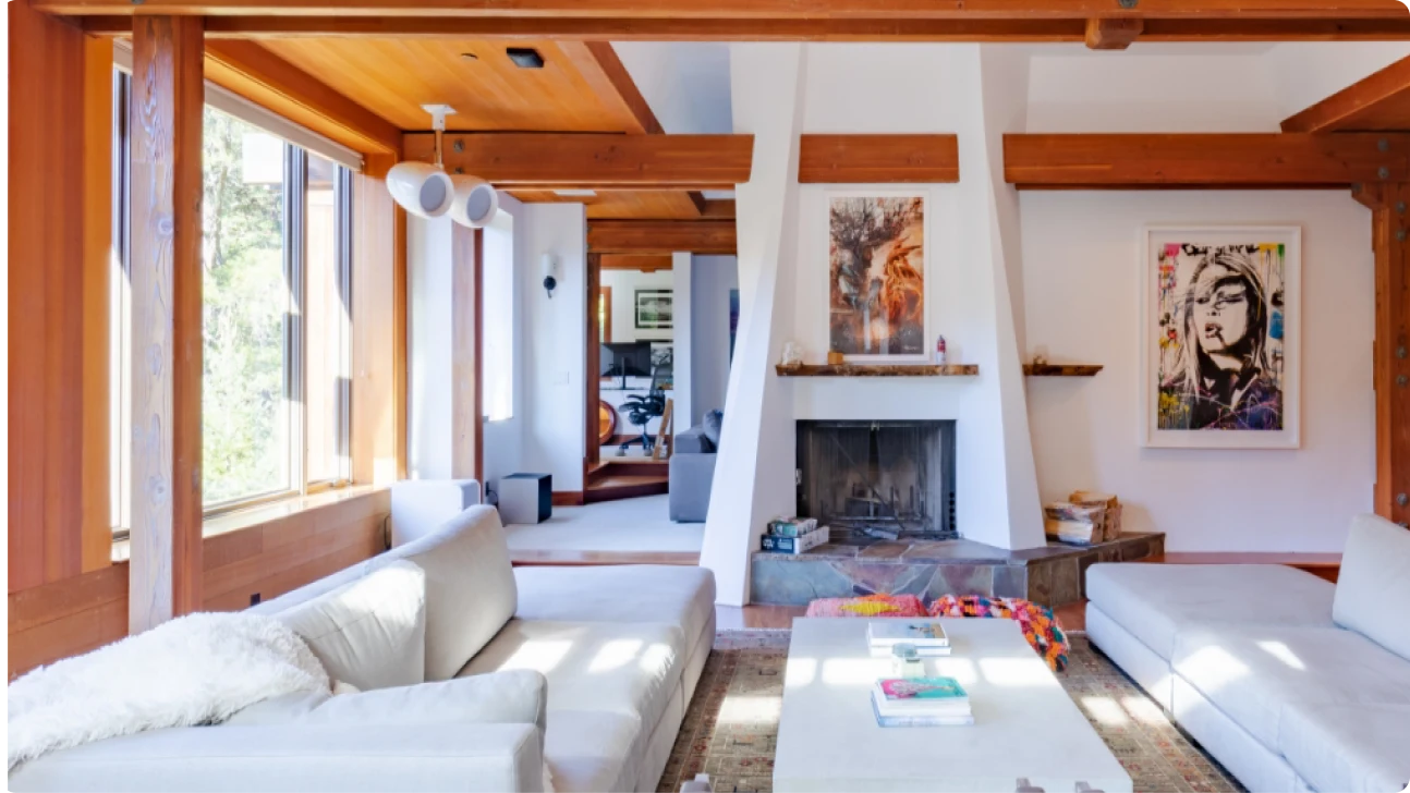Bright living room with exposed wood beams, white plaster fireplace, light upholstery, and art accents in a San Francisco home remodel.