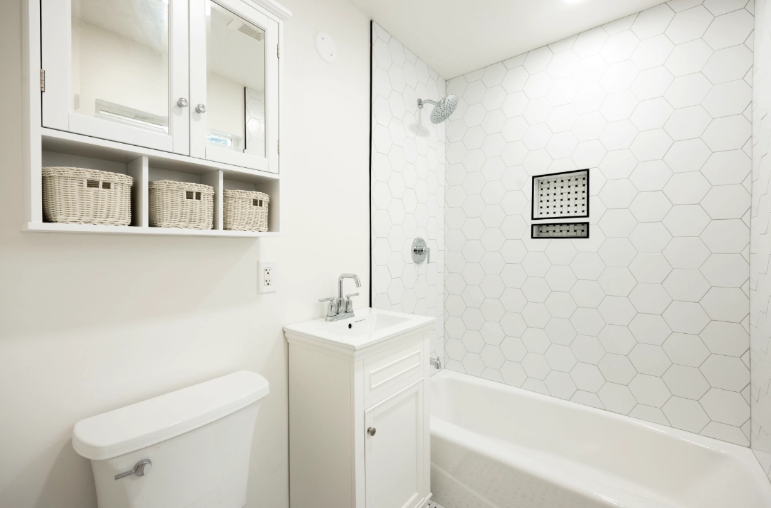 Bright Bay Area bathroom renovation with white hex tile tub surround, compact vanity, chrome fixtures, and open shelving with woven baskets