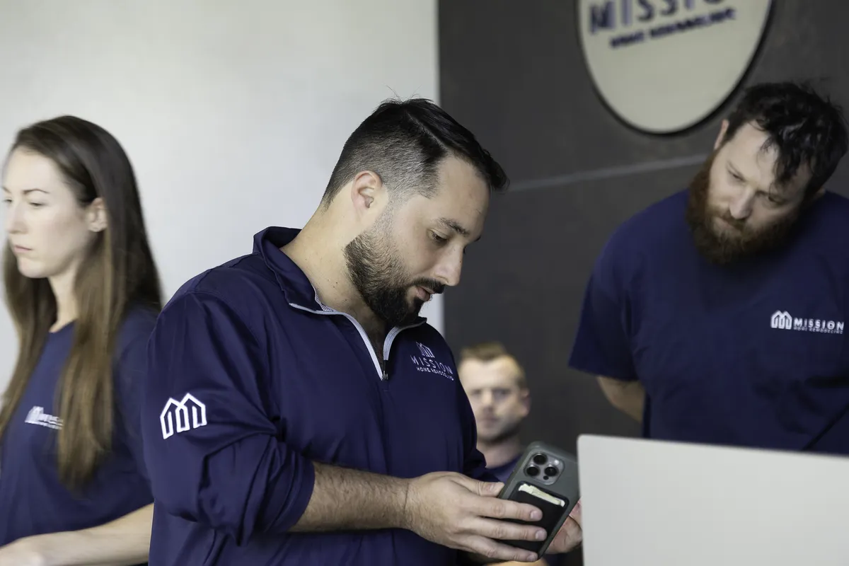 Mission Home Remodeling team members collaborating in the office, wearing branded navy team apparel.