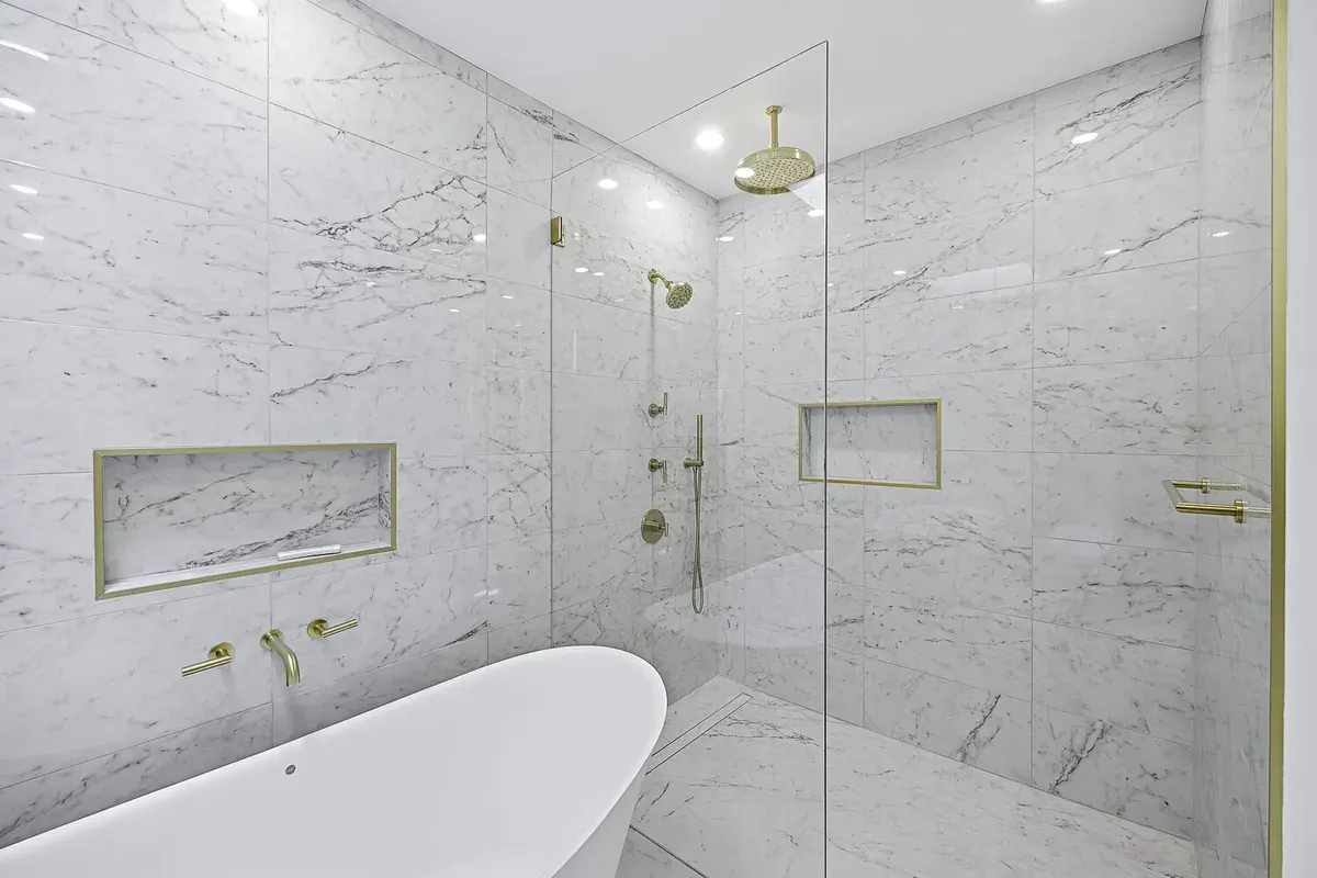 Luxury bathroom with floor-to-ceiling marble, curbless walk-in shower, linear drain, freestanding tub, and brushed brass fixtures.