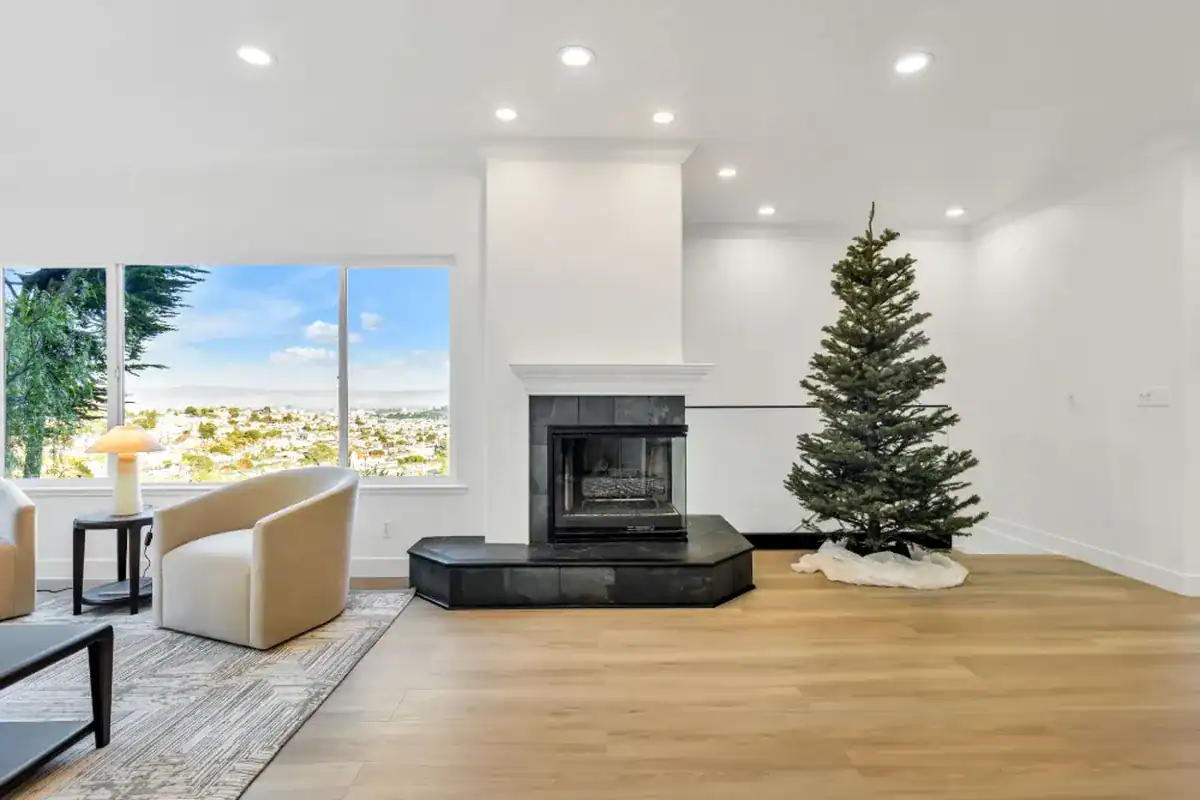 Remodeled living room with a white fireplace surround, black slate hearth, light oak floors, and a wide window overlooking the city.