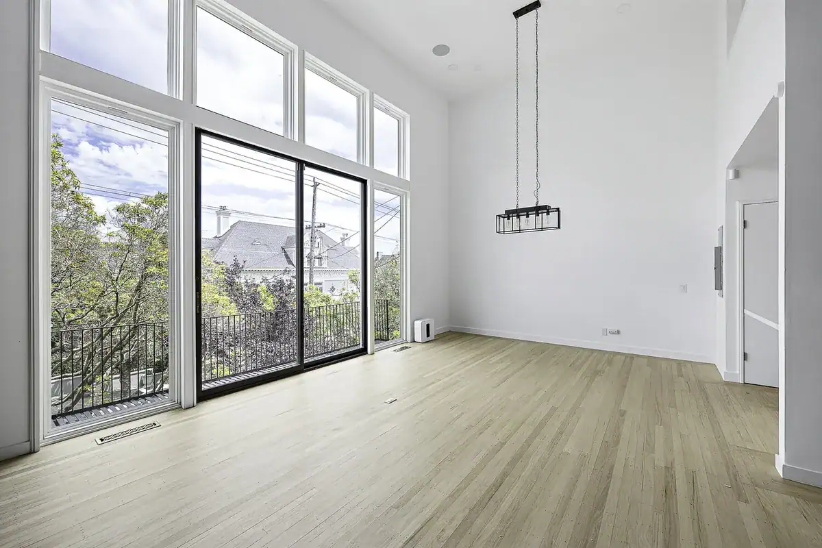 Double-height living room with floor-to-ceiling windows, sliding glass door to a balcony, and light oak floors