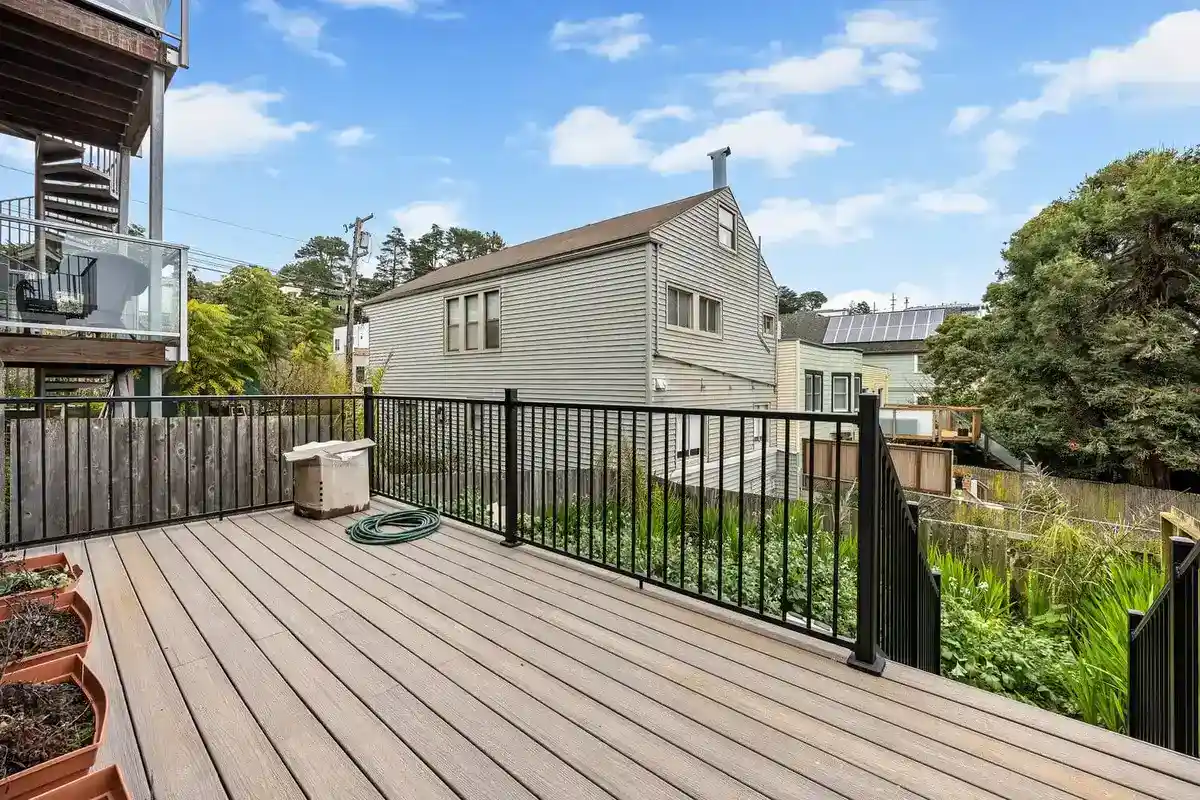 Rear deck with composite decking and black metal railing overlooking a planted backyard and neighboring homes