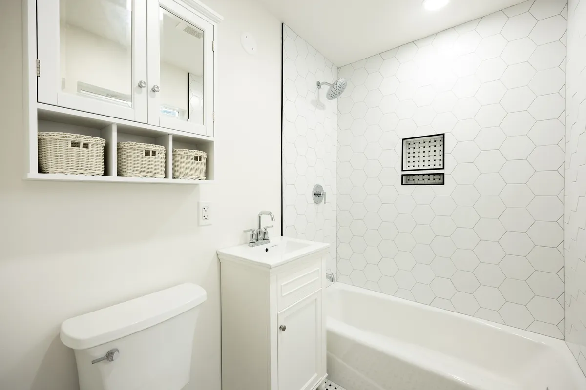 Compact white guest bathroom with a tub-shower combo, white hexagon wall tile with a recessed niche, single-sink vanity, and toilet.