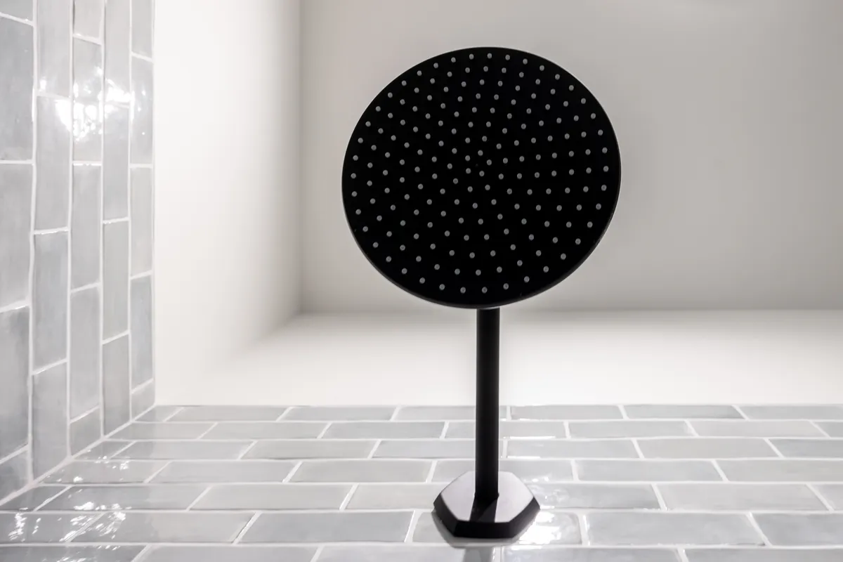 Matte black round rain shower head against gray glazed tile in a remodeled shower.