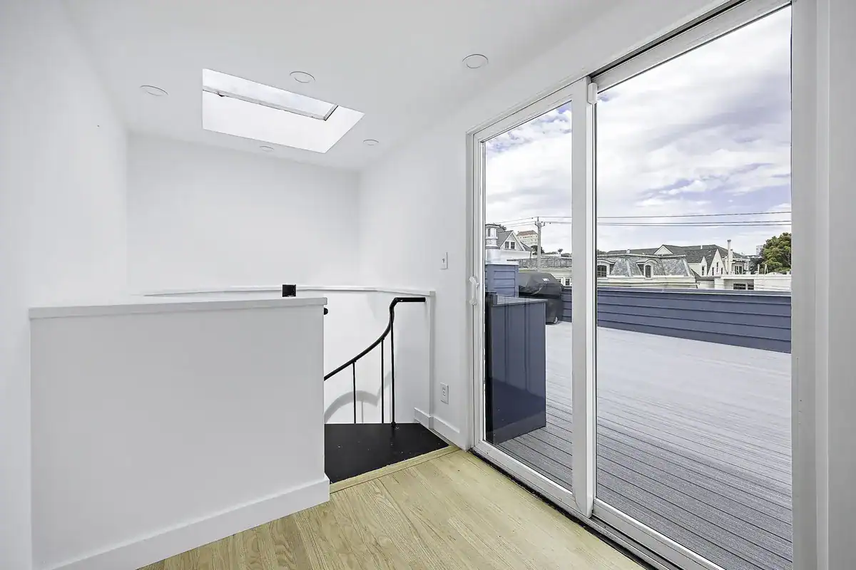Upper-floor landing with a spiral staircase, skylight, and sliding glass door opening to a rooftop deck.