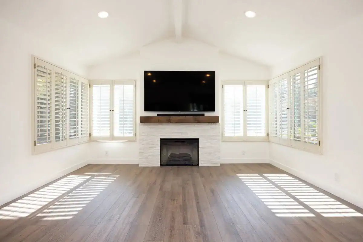 Finished living room with a vaulted ceiling, stone fireplace, plantation shutters, and wood floors in a completed home addition.