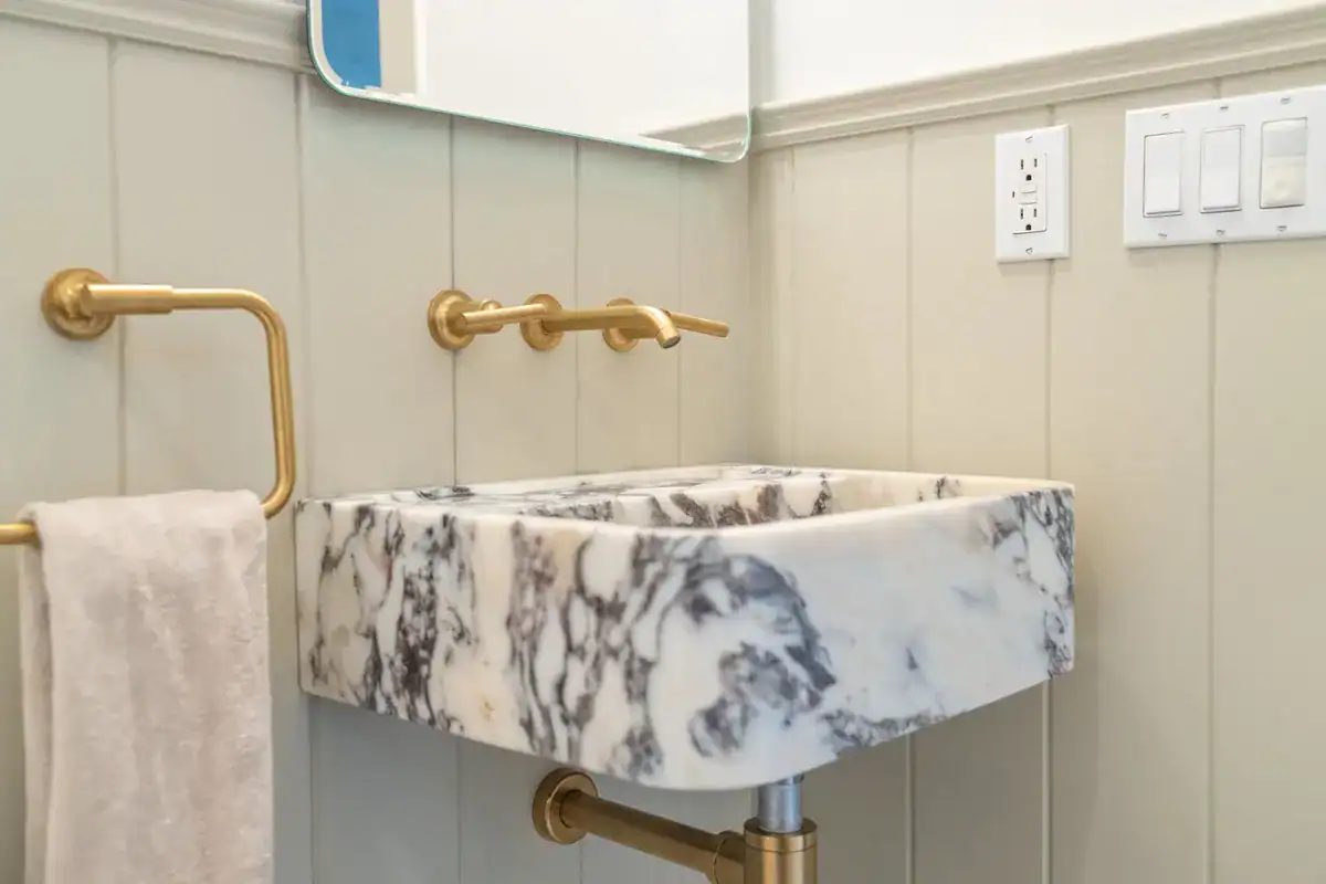 Wall-mounted marble sink with a brass wall faucet and towel ring in a small bathroom with painted vertical paneling