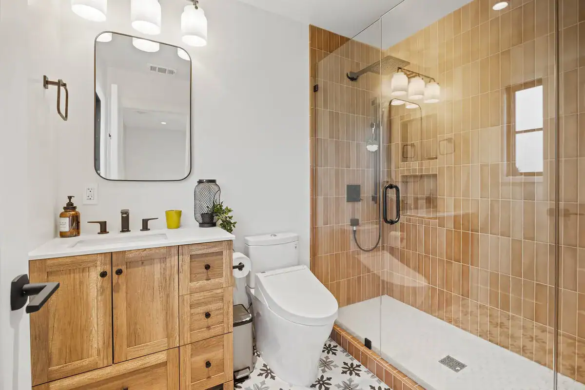Small bathroom with a glass-enclosed walk-in shower, vertical clay-tone tile, and an oak vanity