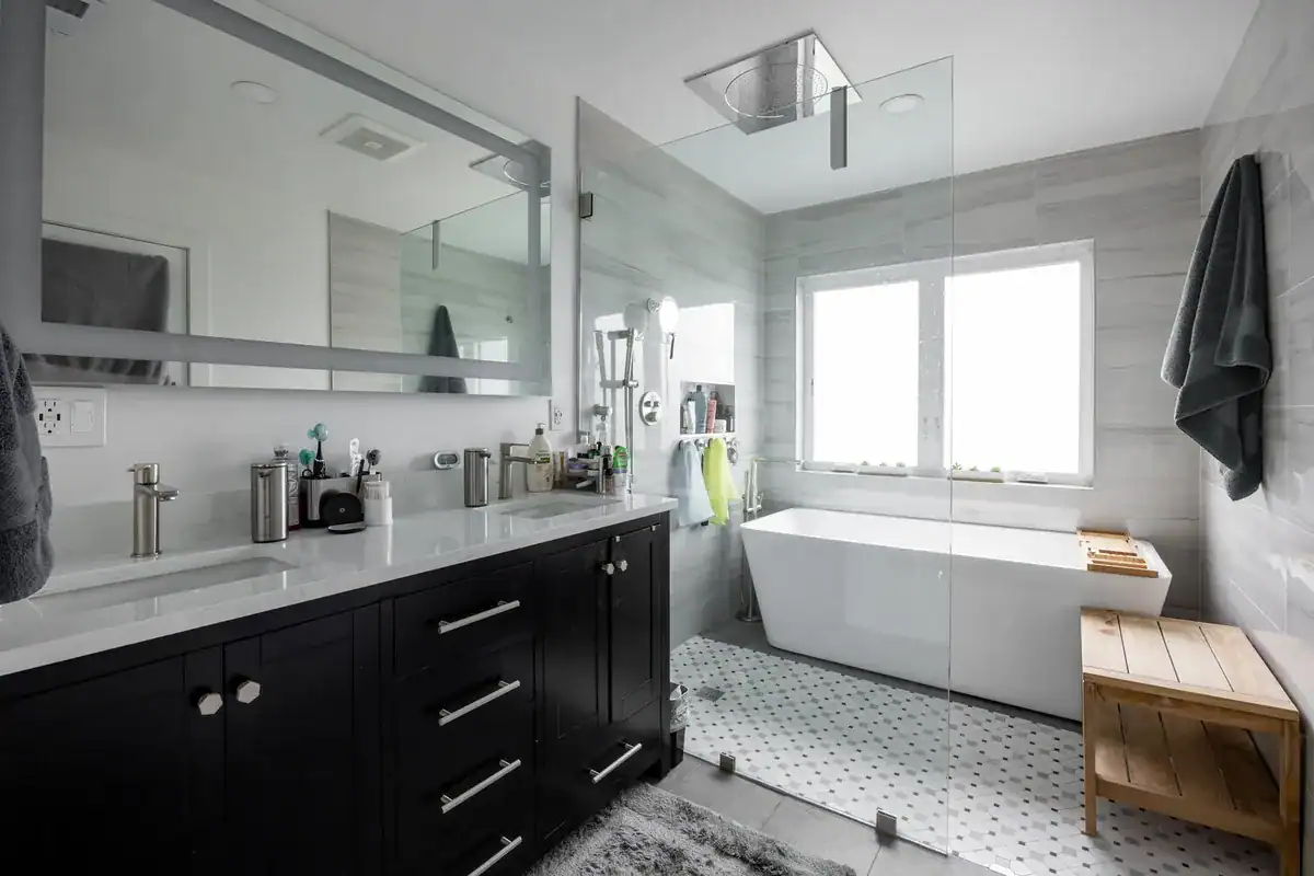 Primary bathroom wet room with a freestanding soaking tub and rainfall shower behind one glass panel
